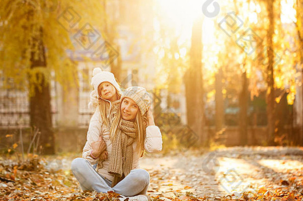 家庭步行。母亲和女儿坐在落叶上。秋天公园。可爱的家庭关系。日落暖色调。