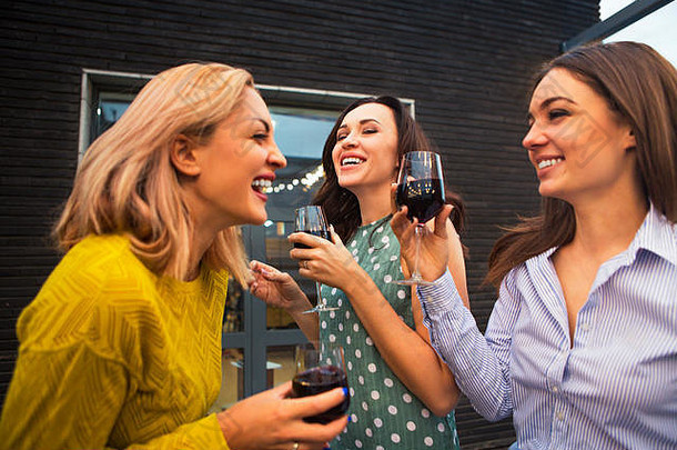 三个年轻快乐的女人笑着，喝着红酒，玩得很开心。党和友谊的概念。
