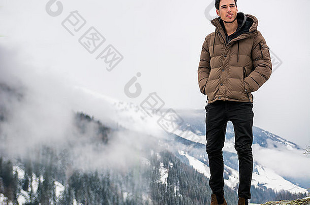 穿着外套的帅哥坐着看镜头。背景上的雪景