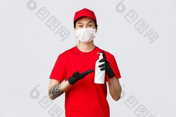 笑容满面的亚洲送货员穿着红色制服，戴着医用面罩和手套。快递员展示洗手液，确保在新冠疫情期间安全运送到家中
