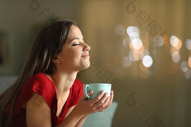 一边视图肖像放松女人休息持有咖啡杯子坐着沙发上首页晚上