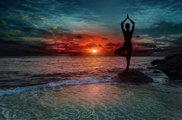 <strong>日</strong>落时在海滩上练习瑜伽的年轻女子的剪影。