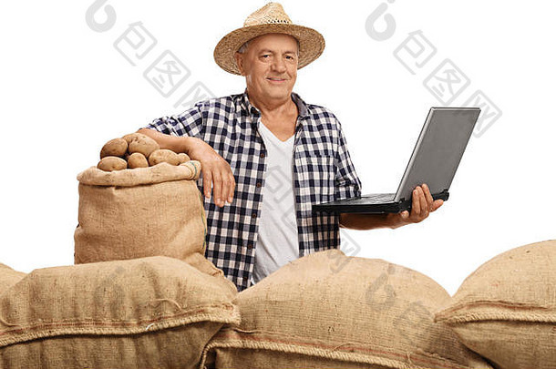 成熟的农民拿着一堆麻袋摆姿势，麻袋里装满了土豆，笔记本电脑被隔离在白色背景上