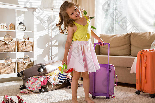 快乐女孩坐着生活房间首页小心翼翼地包装色彩斑斓的夏天衣服玩具行李手提箱旅程孩子
