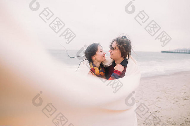 美丽的快乐年轻的夫妇深情地包装白色毯子冬天海背景