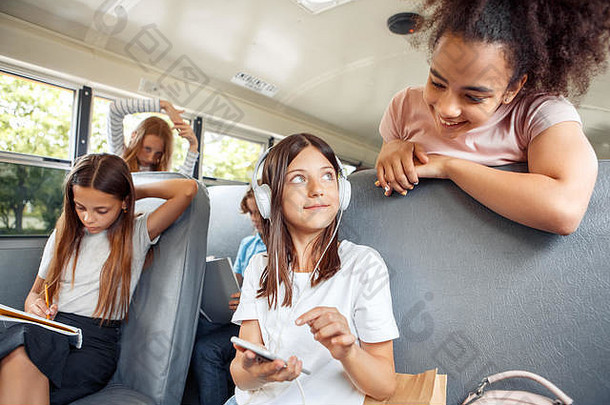 同学们坐公交车上学，女孩戴着耳机近距离坐着，听音乐，朋友唱歌，笑得很开心