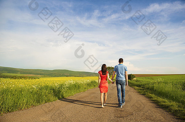 相爱的幸福年轻夫妇手牵手在菜田旁的乡间小路上散步