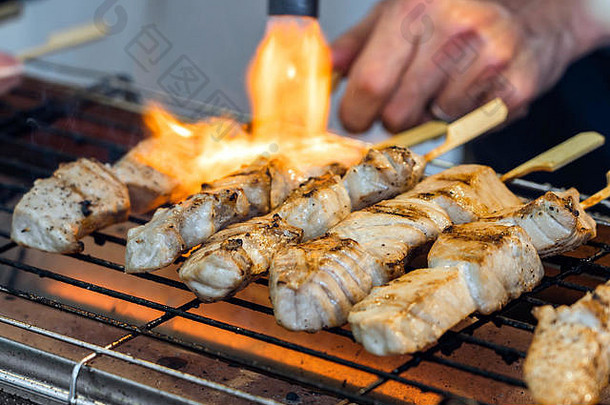 在烤架上制作鱼排的厨师手的特写镜头。一个人正在煮新鲜的金鱼条。火焰正在煎生的金鱼肉