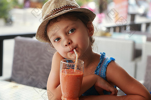 有趣可爱的小女孩在街头餐厅喝着健康的果汁。特写肖像
