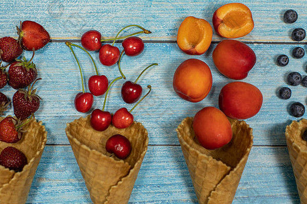 浆果水果冰奶油平躺新鲜的水果蓝莓草莓樱桃杏华夫格锥蓝色的木背景夏天甜蜜的菜单概念自制的冰奶油使