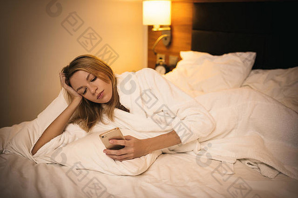 使用智能手机的年轻女子。躺在卧室的床上。