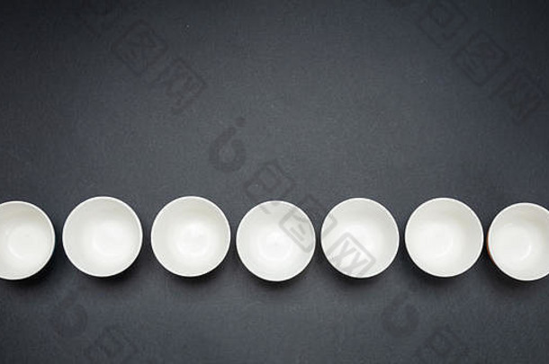 白色干净的陶瓷碗排成一列，黑色背景，空间，俯视图