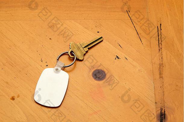 钥匙圈上的空白白色橡胶钥匙，旧木桌上放着一把黄铜钥匙。fob和木材上的空间。