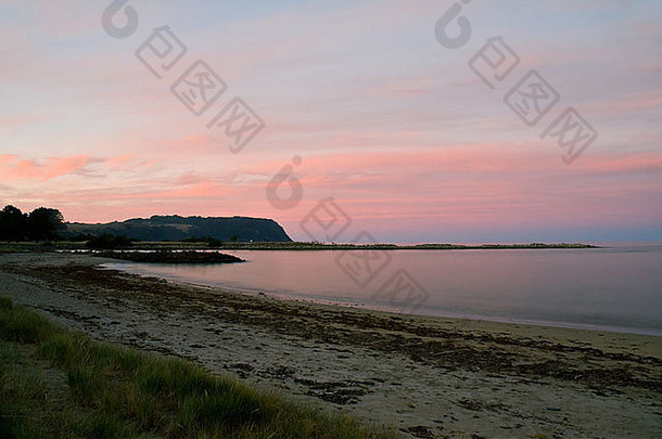 日落后的黄昏在海滩上，随着长时间的曝光，岩石在海洋中形成