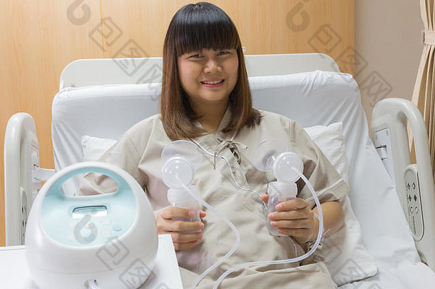 美丽的亚洲母亲在医院病房的病床上拿着吸奶器。
