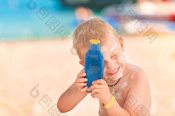可爱的小男孩在海滩上拿着一瓶防晒乳液，身上涂着防晒霜