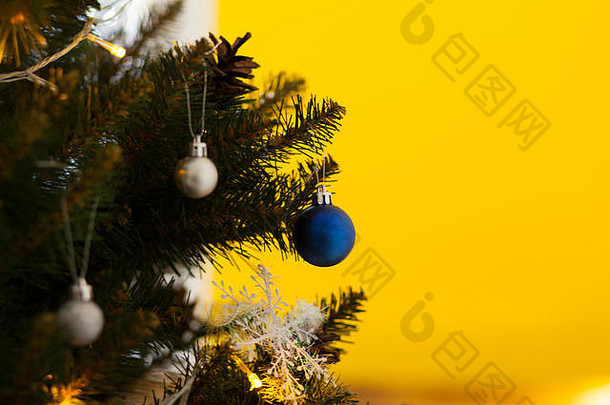 用球和花环装饰的美丽的绿色圣诞树。特写照片。黄色背景