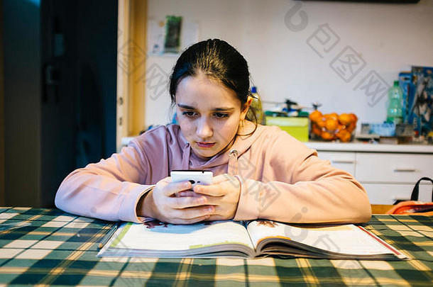 十几岁的女孩在家里厨房的桌子上做作业，帮助自己使用智能手机