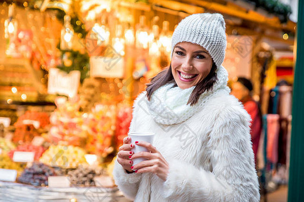 美丽的年轻的女人享受杯加香料的热酒圣诞节市场