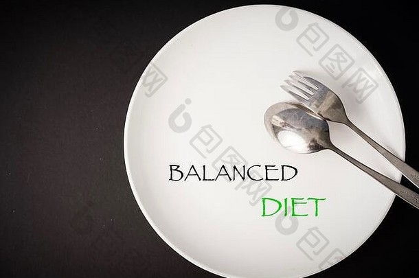 健康饮食观念。用叉子、勺子和卷尺在白色盘子上写上“均衡饮食”字样。