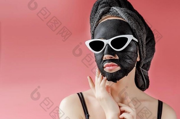 戴眼镜的年轻女士在粉色背景下涂上黑色化妆面料面膜。木炭去皮面膜、spa美容、护肤