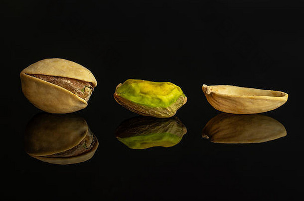 一组两个完整的一片成熟的绿色开心果，在黑色玻璃上隔离成一排