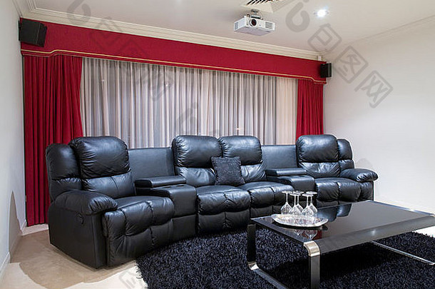 家庭影院房间配有黑色真皮躺椅、红色窗帘、黑色地毯和带酒杯的桌子