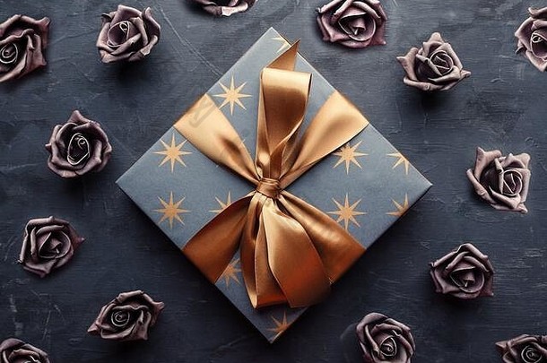 蓝色的礼物盒子黄金丝带弓人工紫罗兰色的玫瑰蓝色的背景