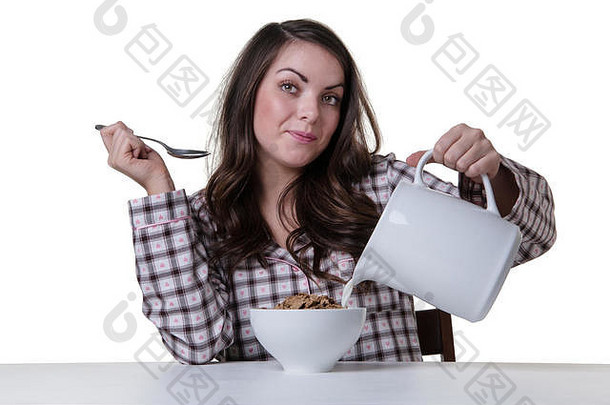 工作室拍摄了一个漂亮的模特坐在桌子旁，端着一碗早餐麦片。普林一手拿着一罐牛奶，泰然自若