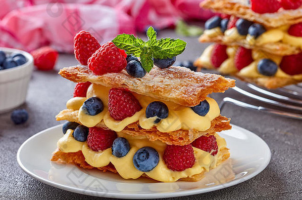 法国甜点米勒福耶，由三块泡芙糕点组成，在混凝土桌上的白色盘子上分层放置奶油冻、覆盆子、蓝莓，