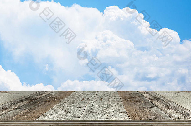 蓝天下的空木制桌面上有蓬松的白云，用于放置食物或产品