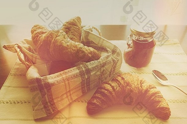 草莓酱小罐，面包篮，羊角面包，条纹布和银勺。温暖、复古的色调。