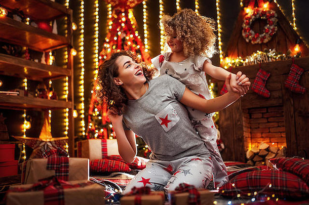 快乐可爱的卷发小女孩和她的姐姐礼物。姐妹们在室内圣诞树旁玩耍。在圣诞节房间里用礼物爱家人。