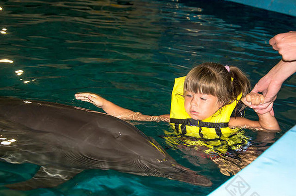 小女孩和海豚在夜间游泳池里游泳