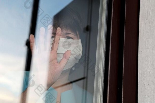戴着医用面罩的女人透过窗户玻璃看。Quarantine在CV2019冠状病毒疾病中的流行