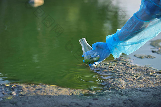 特写环境保护主义者的手，一名研究人员正在从一个湖泊中采集污染水样本