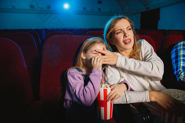 白人母亲和女儿在电影院、房子或电影院看电影。看起来富有表情、惊讶和情绪化。一个人坐着玩。关系，爱情，家庭，童年，周末。