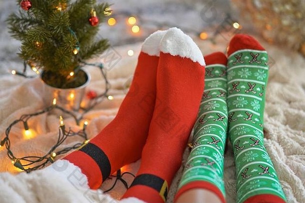 在圣诞树附近穿圣诞袜的脚。这对夫妇坐在毯子旁，穿着羊毛袜子热身。冬季和圣诞节