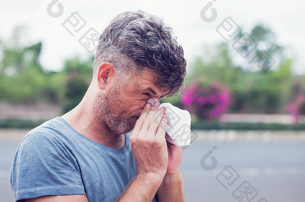 男人在户外用纸巾打喷嚏。花粉过敏，春天。