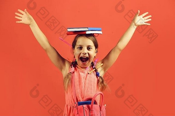 女孩手里拿着红色和蓝色的书。女学生面带微笑，举起<strong>双</strong>手，孤立地站在<strong>红色背景</strong>上。学生穿着粉红色的连衣裙，带着彩色铅笔和辫子。返校概念