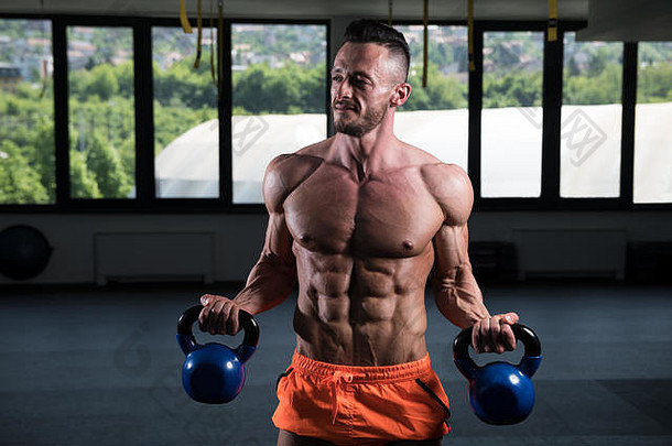 男子在黑暗的健身房里用壶铃锻炼身体-健美运动员用壶铃做重量级运动
