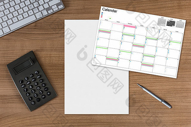 木制桌子上的日历和白色床单，配有计算器、现代键盘和银笔