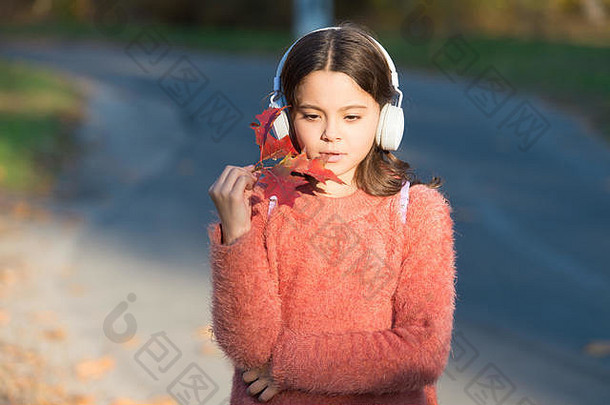 音乐为秋天带来温馨的心情。听歌曲。好心情的旋律。按歌驾驶。秋天温暖的日子里，在户外欣赏音乐。音频文件。孩子女孩放松秋叶与现代无线耳机。