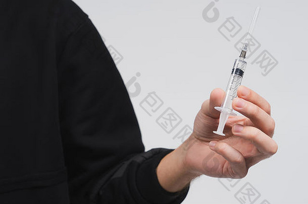 男人的手拿着装有液体的注射器。一个穿着白色背景的黑色连帽衫的家伙。提供药物或医疗服务的人。者。