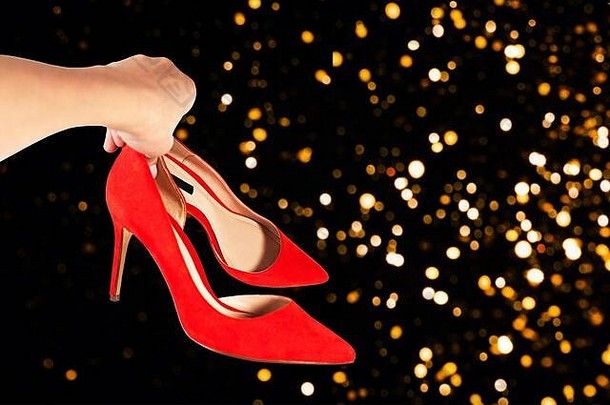 在散焦抽象的圣诞派对背景上，这位女士手里拿着时尚的红色鞋子。情人节，新年派对贺卡的概念。