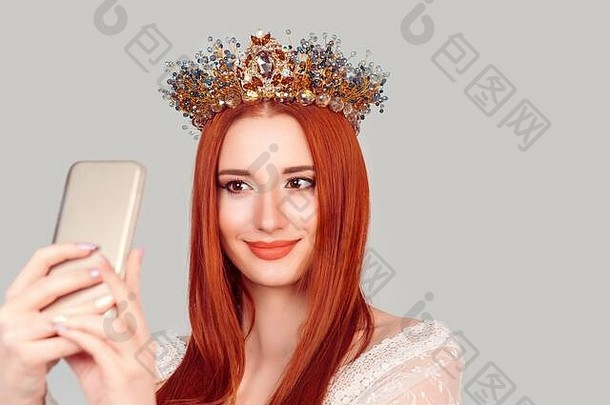 自画像。穿着白色蕾丝连衣裙的年轻选美皇后用智能手机和头戴水晶王冠的微笑美女自拍