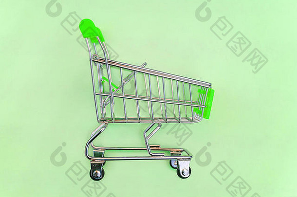 小型超市购物车，用于购物玩具，带有轮子和绿色塑料元件，背景为绿色柔和的彩色纸张。购物的概念。广告空间