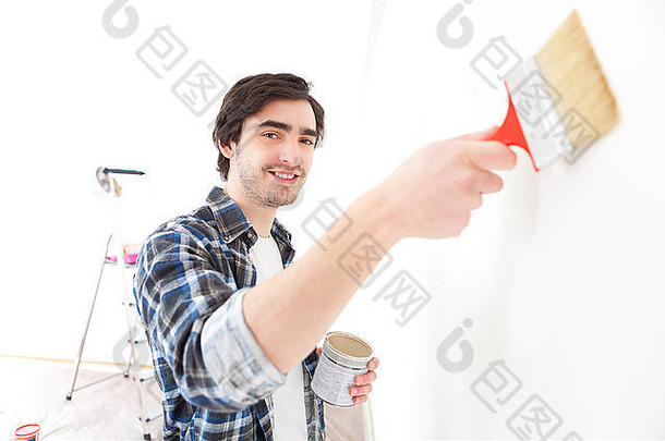 一个迷人的年轻人在他的新公寓里粉刷墙壁的画面