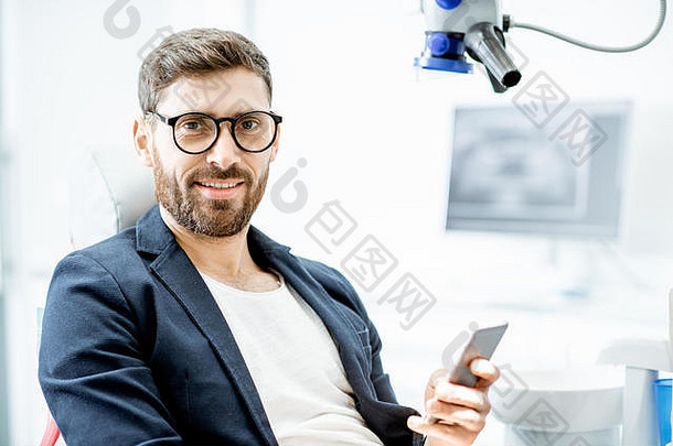 一位英俊商人的肖像，手机坐在牙科办公室的牙科椅上