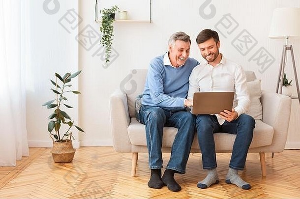 成年儿子教高年级父亲坐在室内使用笔记本电脑